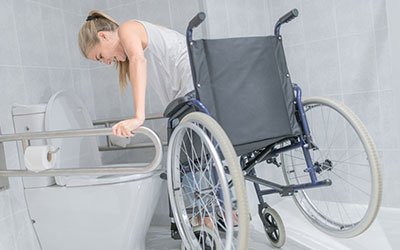 Image of a woman leaning on a bathtub from a wheelchair, highlighting accessibility challenges addressed in the context of physical rehabilitation.