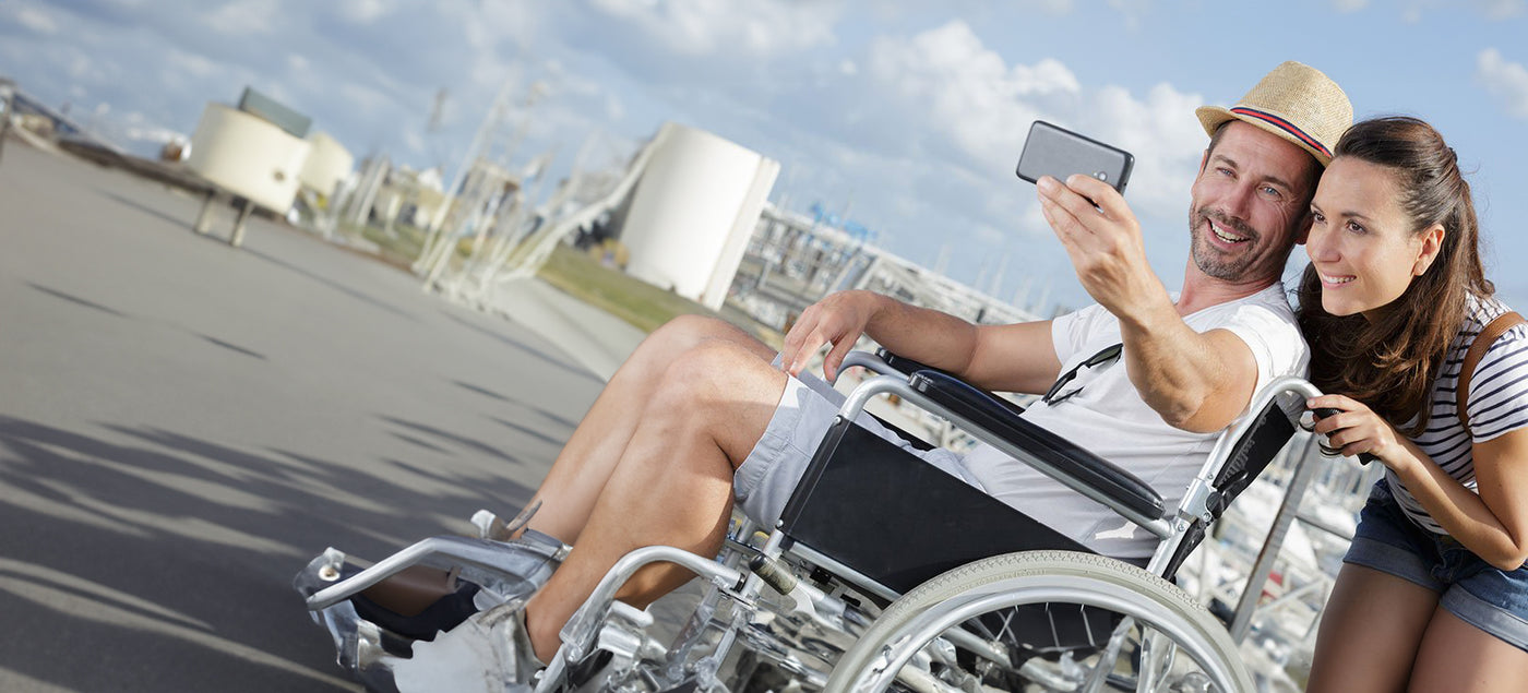 Banner image for a travel guide with a smiling couple, the man in a wheelchair, taking a selfie, with a note on consulting healthcare professionals for personalized advice.