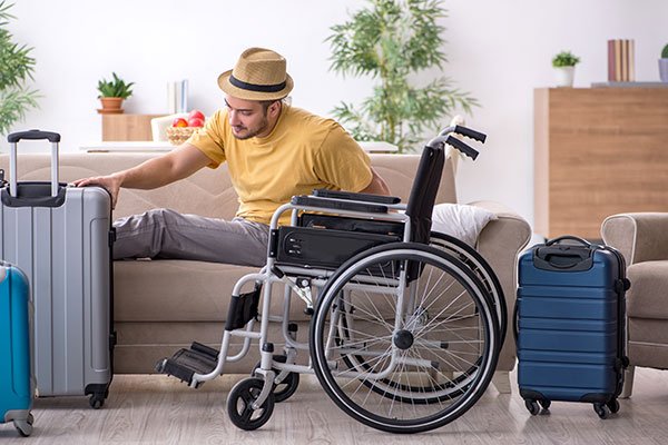 Image of a man in a wheelchair reaching for a suitcase, with the enthusiastic caption "Let's get packing!" indicating preparation for travel.