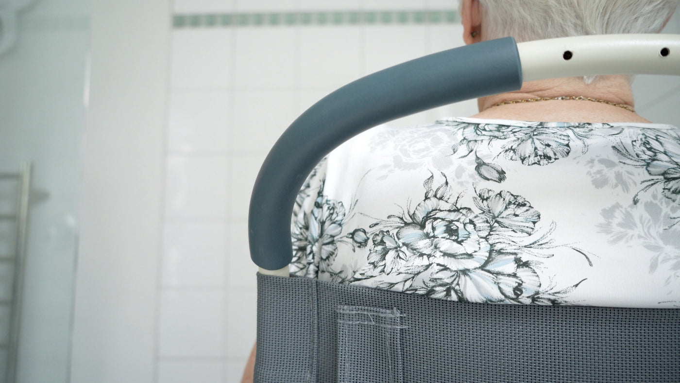 Close-up of a senior person's back, using a Showerbuddy chair with a floral design, on a webpage promoting bathroom mobility solutions.
