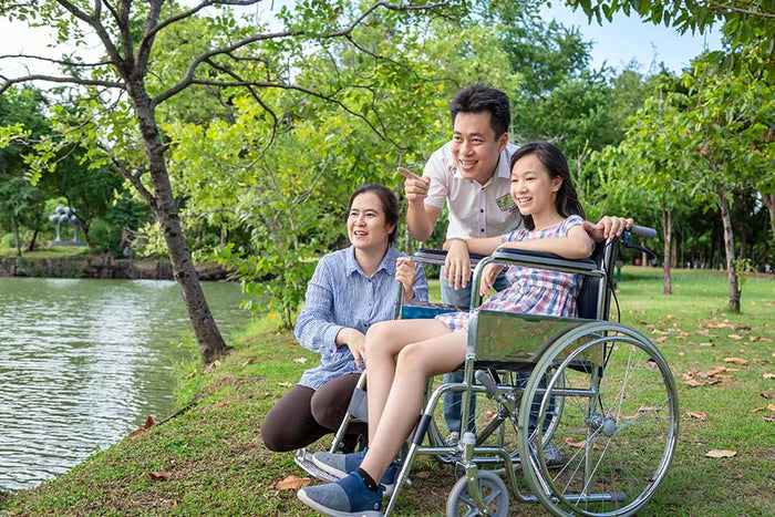Image of three family members in a park, one in a wheelchair, smiling and enjoying time together.