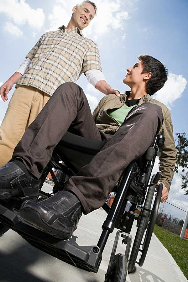 Image of a smiling adult in a wheelchair engaging with a standing person.