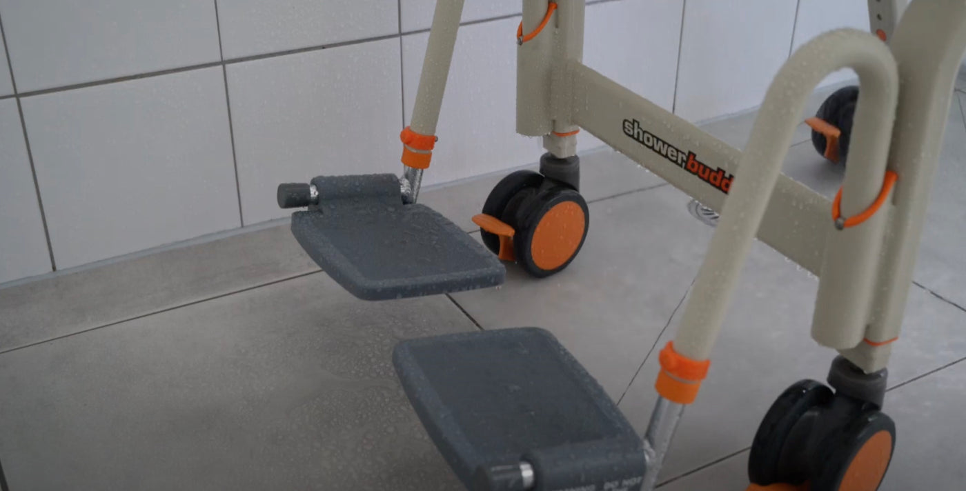 Close-up of the Showerbuddy chair's footrest and wheels, highlighting the textured surface for grip and the sturdy, maneuverable design for safe bathroom navigation.