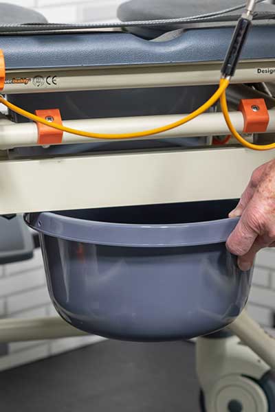 Image of a hand removing the commode bucket from a Showerbuddy chair, highlighting the feature of a removable bucket for convenience.
