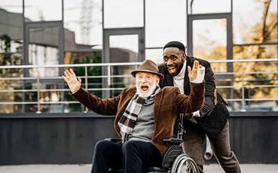 A joyful image featuring an elderly person in a wheelchair and a companion, both laughing and gesturing excitement.